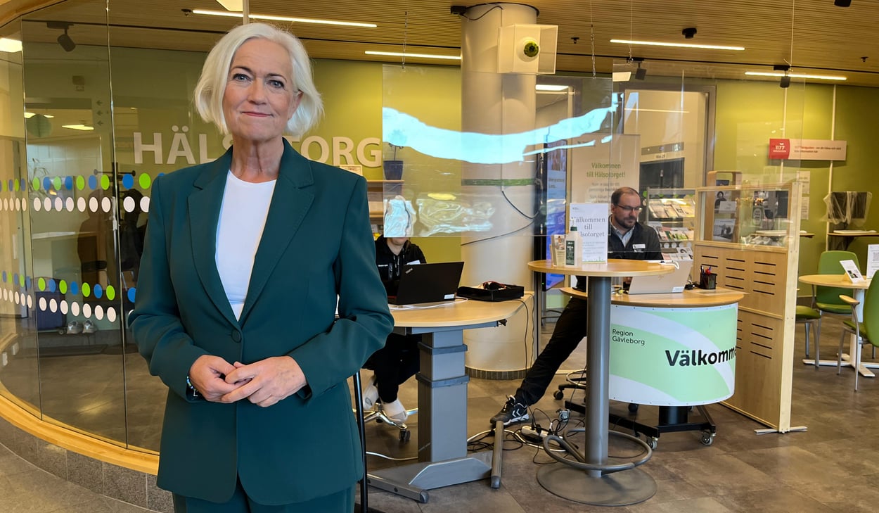 Sjukvårdsminister Acko Ankarberg Johansson (KD) under hennes besök på Gävle sjukhus, här med hälsotorget i bakgrunden. Hon är medelålders, vitt hår i pagefrisyr samt bär vit t-shirt och skogsgrön kostym. 