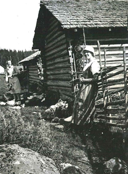 Ett svartvitt foto av en person som st&aring;r framf&ouml;r en stuga.