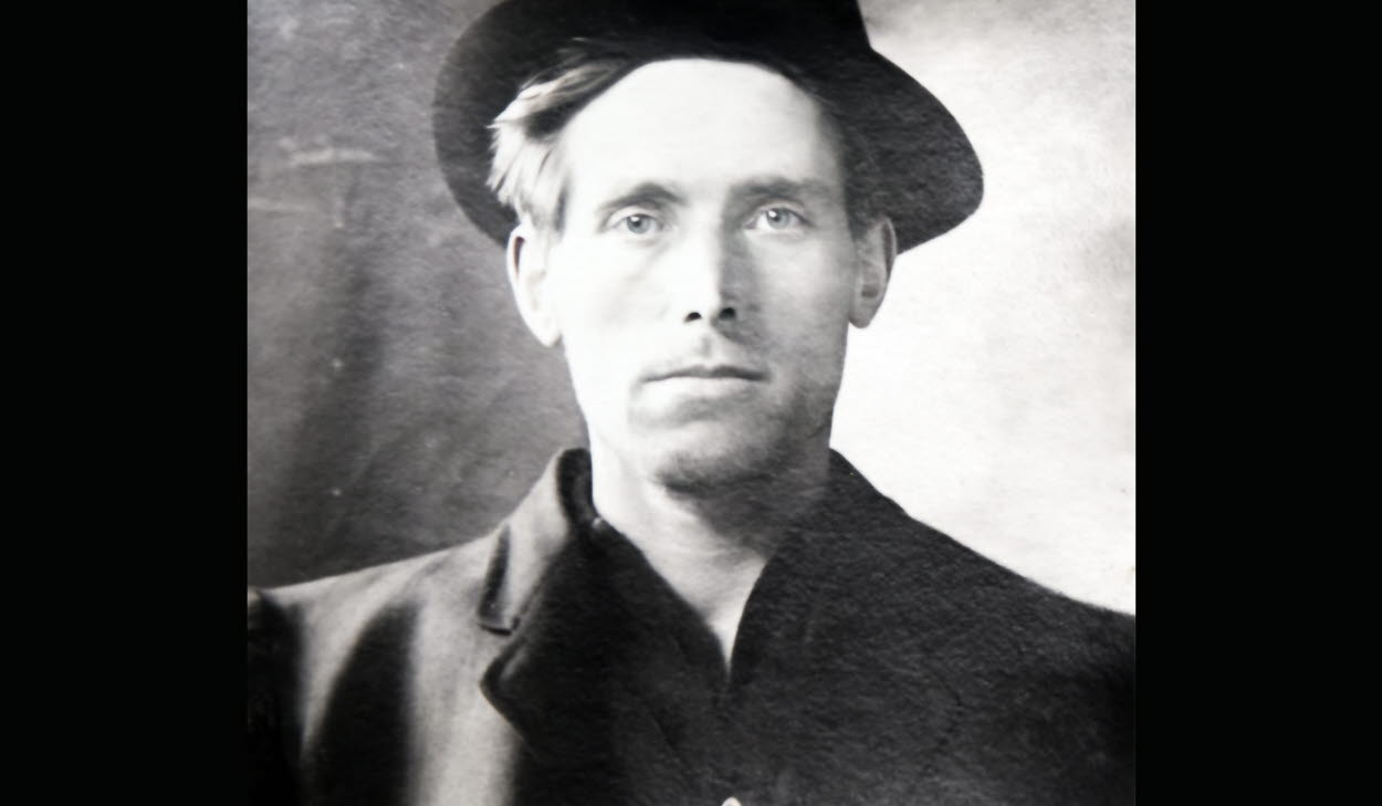 Svartvit bild av författare Joe Hill iklädd rock och hatt.