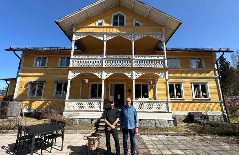 Två personer utanför stort gult hus