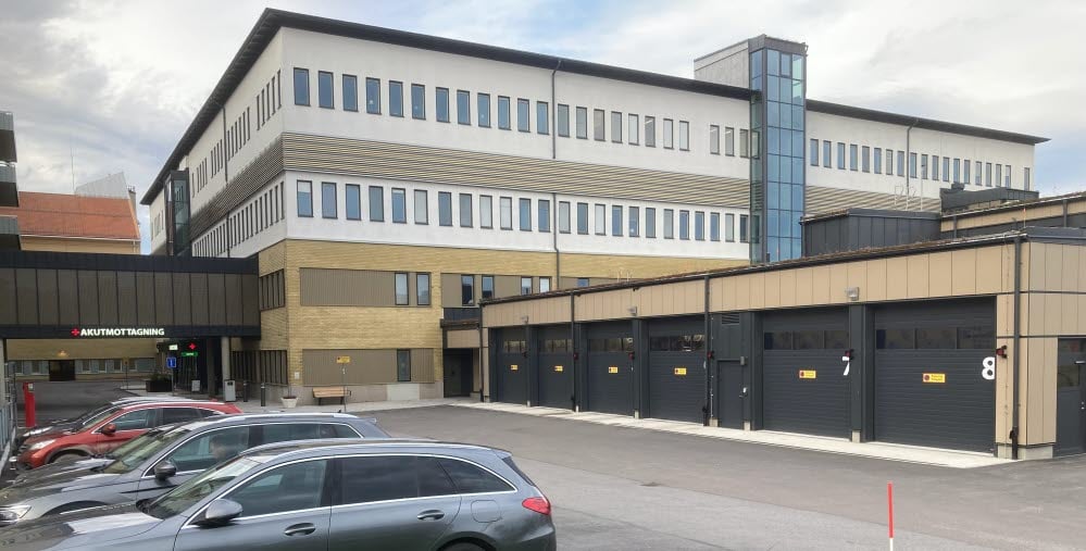 Hus 07/08 på Hudiksvalls sjukhus. I förgrunden syns portarna till ambulansintaget och i bakgrunden syns ingången till akutmottagningen. Bilar är parkerade i förgrunden.