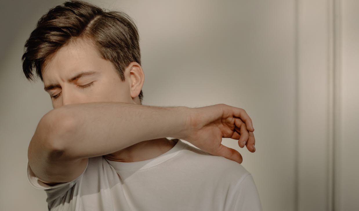 Person som verkar vara förkyld och nyser i armvecket.