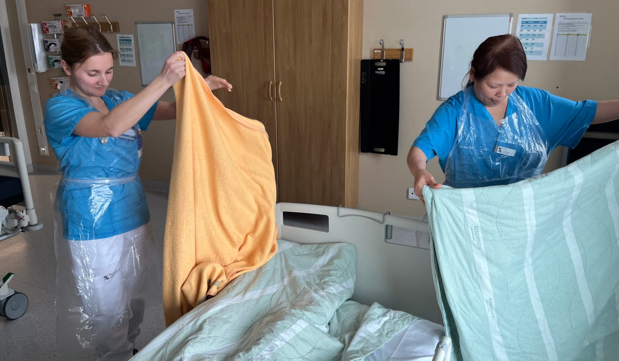 Två vårdpersonal i patientsal, bäddar säng.