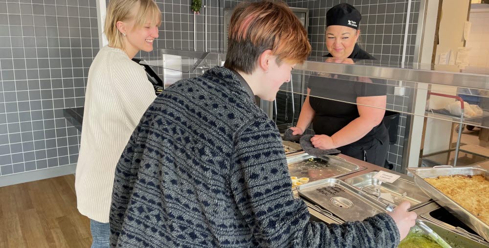 Tre personer i Bollnäs folkhögskolas nyrenoverade restaurang. Två personer tar mat och en personal står bakom disken.