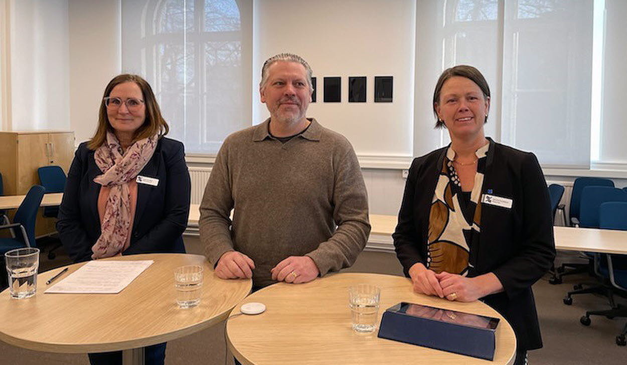 Tre personer står bakom höga ståbord.