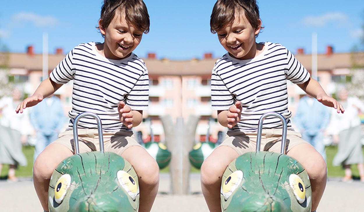 Barn som leker på en gunga med hus i bakgrunden