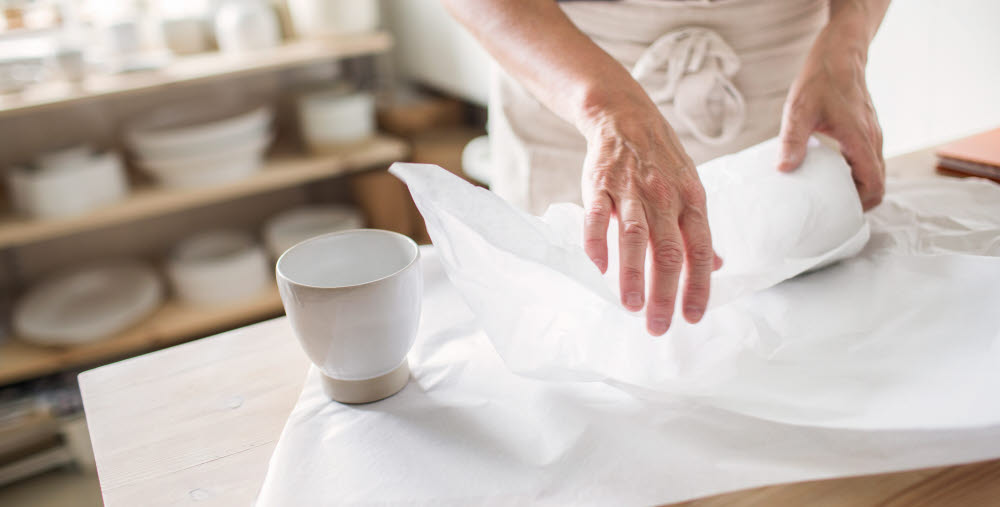 Närbild på ett par händer som slår in keramik.