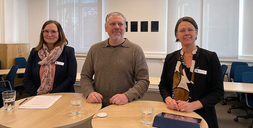 Tre personer står bakom höga ståbord.